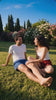 A couple sitting on a sunlit lawn, laughing together, in matching KAYA cotton loungewear
