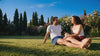 A couple sitting on a sunlit lawn, laughing, in matching KAYA cotton loungewear