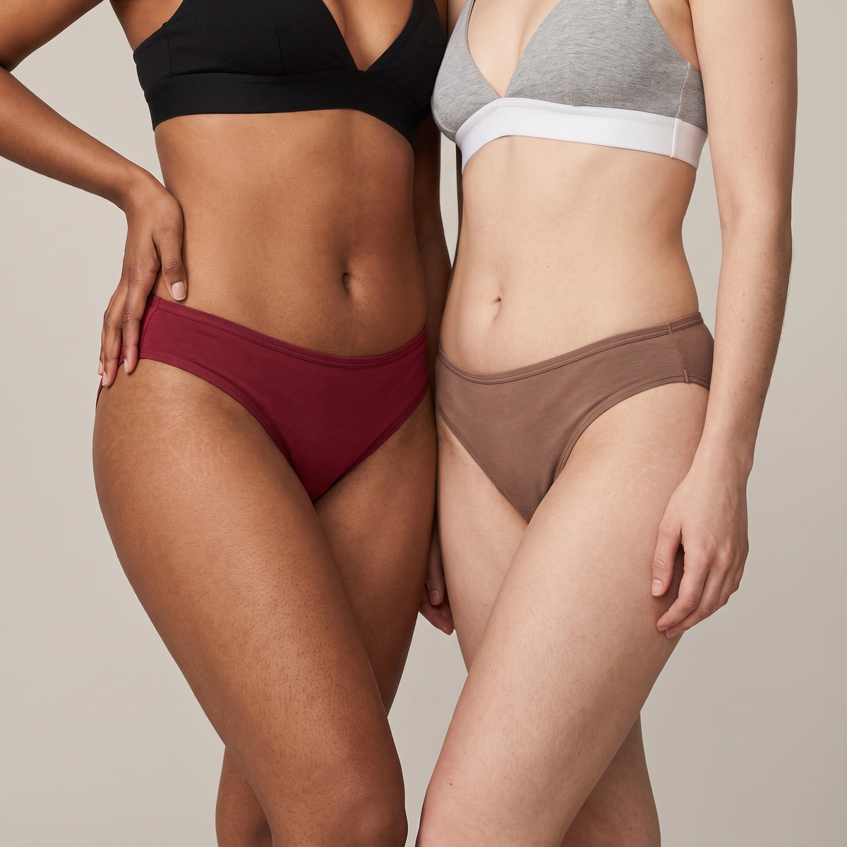 Two women side by side in KAYA cotton bikini briefs — cherry red with a black triangle bra, and mocha with a heather-grey triangle bra